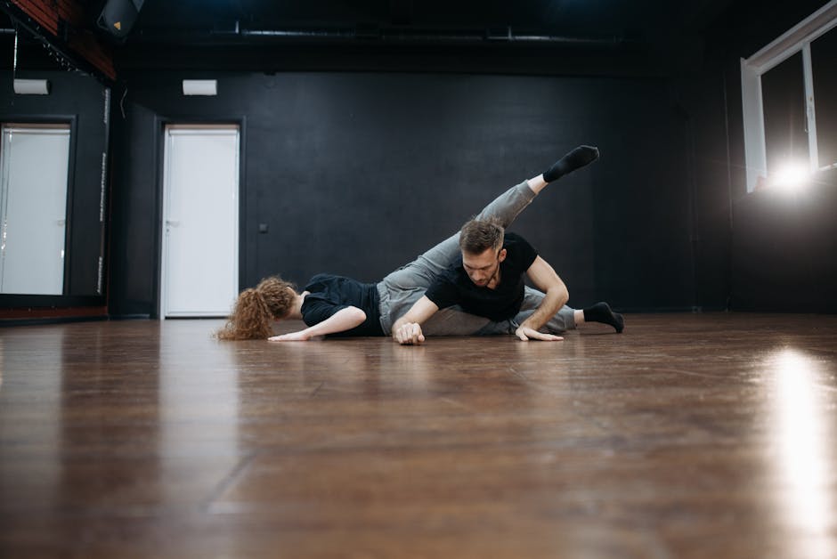 Male and female dancers performing a contemporary routine on a wooden floor in a studio.